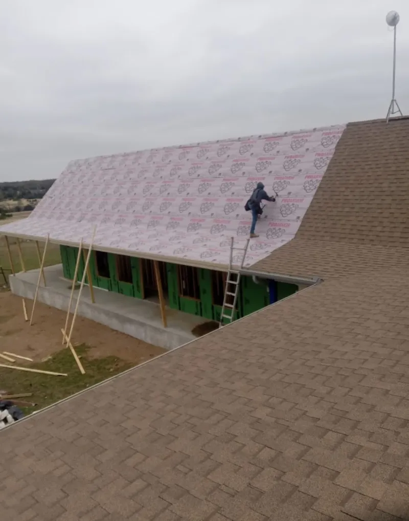 Worker preparing underlayment for a metal roof installation in Howland Center